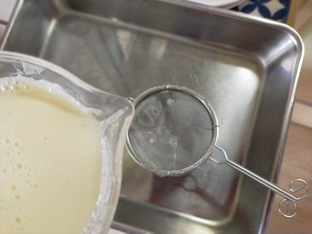 茶こしを使ってバットに流し込まれる豆乳